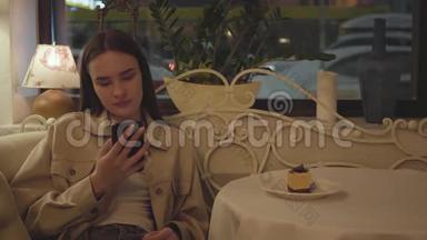 漂亮的女孩<strong>坐在餐馆</strong>的桌子上用手机发短信。 这块美味的蛋糕在桌子上